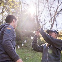 a man and a woman setting up string lights outdoors