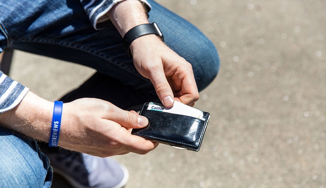 A person casually dressed in denim jeans pulls a key finder from their wallet