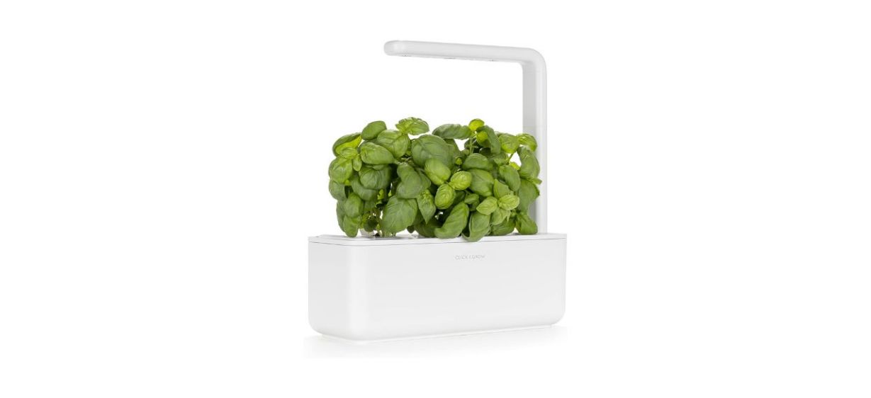 White indoor herb garden with basil growing in it and a grow light